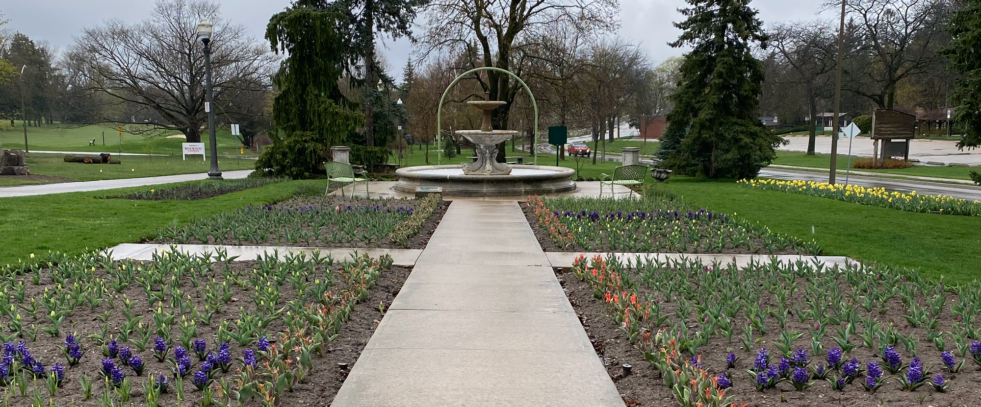 sidewalk leading to fountains with flowers on either side
