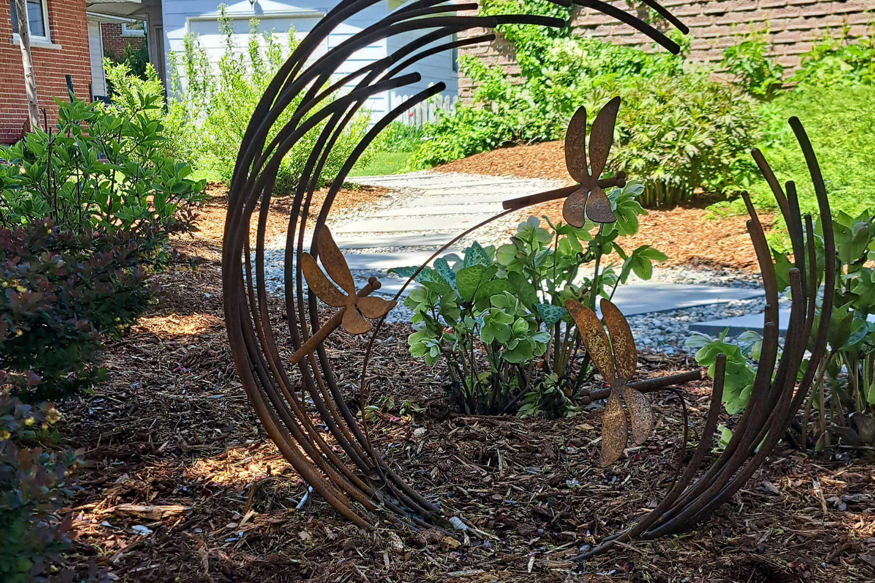 a circular iron sculpture in a mulched garden bed