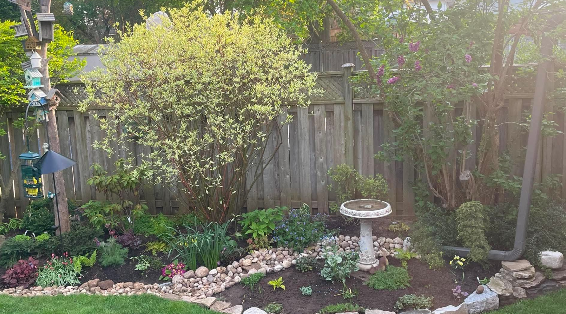 A backyard garden featuring stonework a bird bath, and bird feeders.